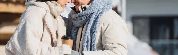 Vue recadrée d'un jeune homme heureux tenant une tasse en papier près d'une petite amie joyeuse, bannière — Photo de stock