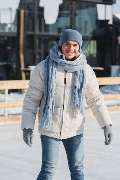 Jovem feliz em cachecol, chapéu de inverno e patins de gelo patinação fora — Fotografia de Stock