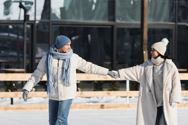 Junges und glückliches Paar hält Händchen beim Schlittschuhlaufen auf der Eisbahn — Stockfoto