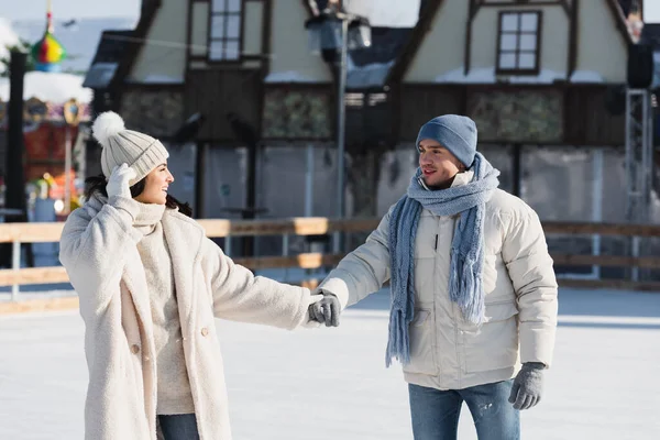 Young and cheerful couple holding hands while skating on ice rink — Stock Photo