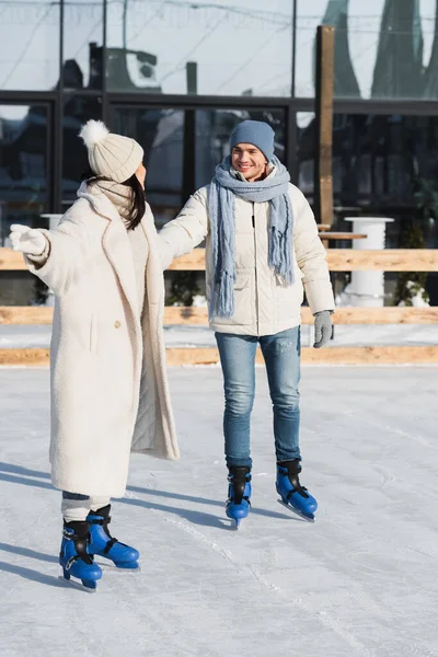 Full length of young and happy couple holding hands while skating on ice rink — Stock Photo