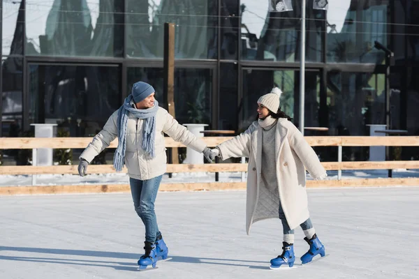 Toute la longueur du jeune couple en tenue d'hiver tenant la main tout en patinant sur la patinoire — Photo de stock