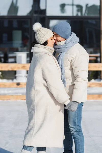 Young couple in winter hats holding hands while kissing outside — Stock Photo