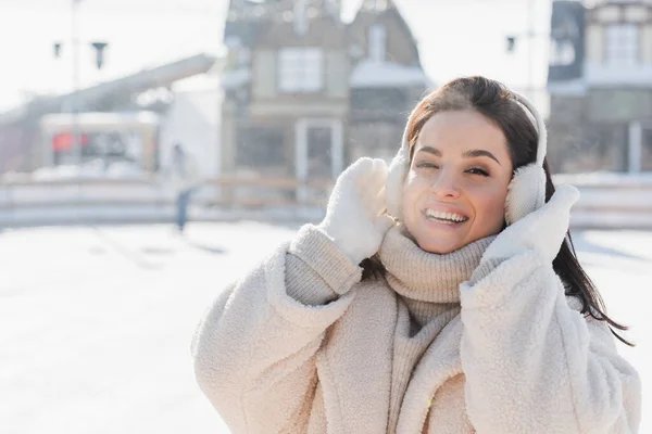 Jeune femme heureuse ajustant les cache-oreilles à l'extérieur — Photo de stock