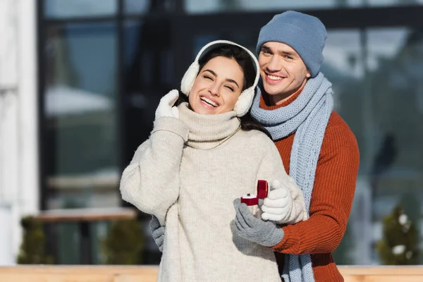 Young man holding box with wedding ring near cheerful woman outside — Stock Photo