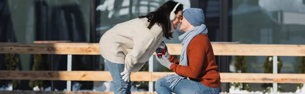 Glücklicher Mann hält Schachtel mit Ehering und kniet, während er der Frau auf der Eisbahn einen Heiratsantrag macht, Banner — Stockfoto