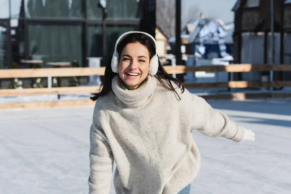 Весела молода жінка в светрі і вухах катається на ковзанах — стокове фото