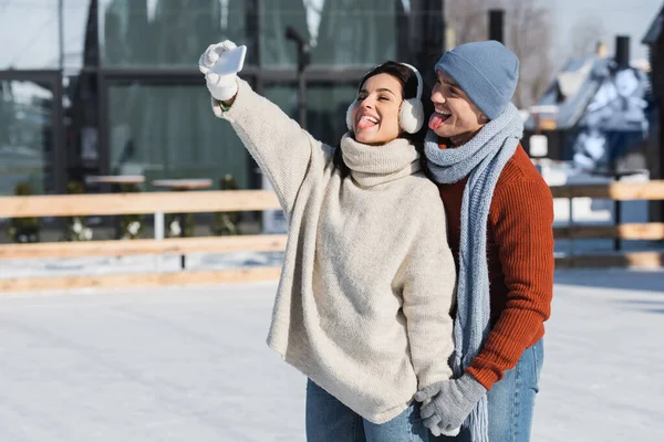 Happy couple sticking out tongues while taking selfie on ice rink — Stock Photo