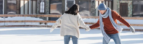 Jeune femme dans des cache-oreilles tenant la main avec petit ami sur la patinoire, bannière — Photo de stock