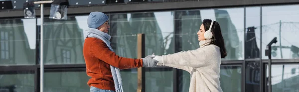 Mujer joven en orejeras cogidas de la mano con el novio fuera, pancarta - foto de stock