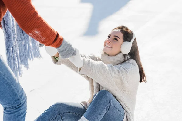 Homem de luvas ajudando a sorrir namorada levantar-se no ringue de gelo — Fotografia de Stock