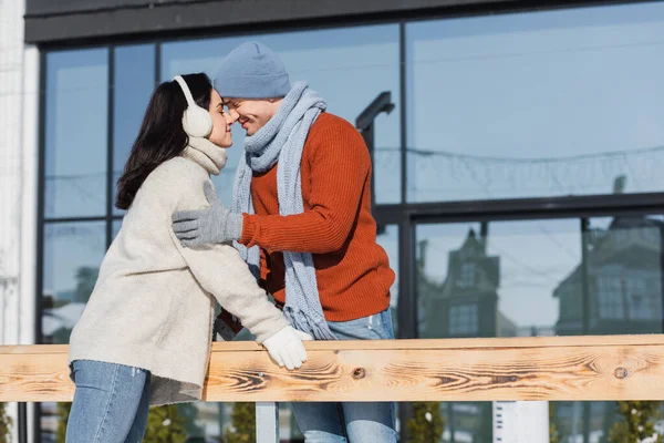 Happy couple smiling while hugging near wooden border on ice rink — Stock Photo