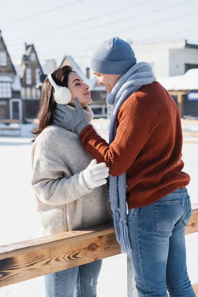 Side view of cheerful couple kissing near wooden border on ice rink — Stock Photo