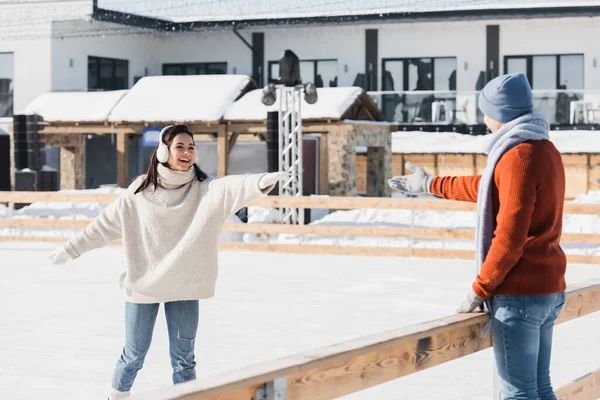 Jeune femme souriante en patins à glace patinant avec la main tendue près du petit ami — Photo de stock