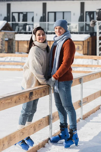 Full length of happy couple standing near wooden border on skating rink — Stock Photo