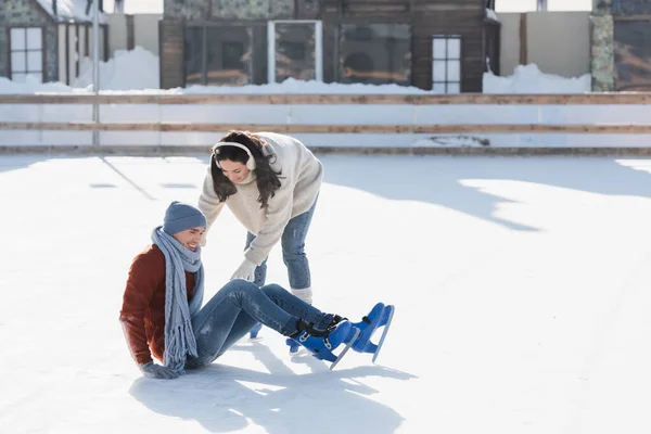 Volle Länge des lächelnden Mannes, der beim Schlittschuhlaufen auf der Eisbahn neben Frau fällt — Stockfoto