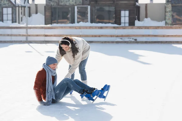 Full length of smiling man falling near woman while skating on ice rink outside — Stock Photo
