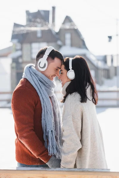 Vista lateral de casal sorridente abraçando enquanto ouve música em fones de ouvido fora — Fotografia de Stock