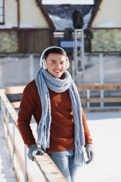 Smiling young man in sweater and scarf listening music outdoors — Stock Photo