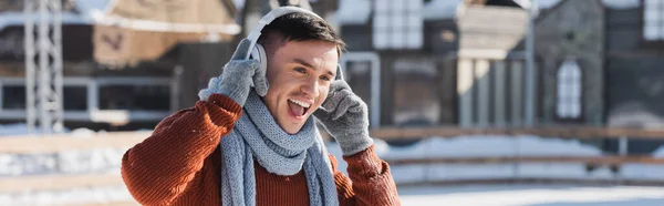 Positive young man in sweater and scarf listening music while singing outside, banner — Stock Photo