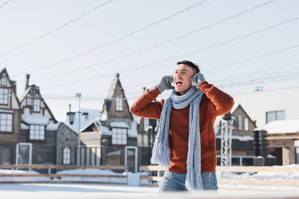 Positive young man in sweater and scarf listening music while singing outside — Stock Photo