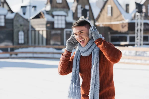 Heureux jeune homme en pull et écharpe écouter de la musique tout en chantant à l'extérieur — Photo de stock