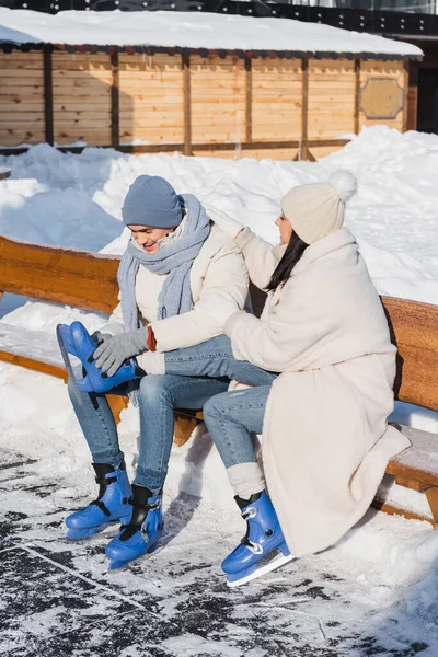 Sorrindo jovem casal em chapéus de inverno sentado no banco e vestindo patins de gelo — Fotografia de Stock