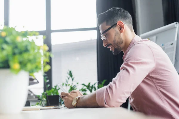 Vista lateral del hombre de negocios musulmán utilizando el teléfono inteligente en la oficina - foto de stock