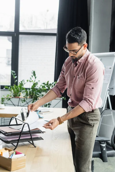 Muslimischer Geschäftsmann durchsucht Papiere auf Tisch im Büro — Stockfoto