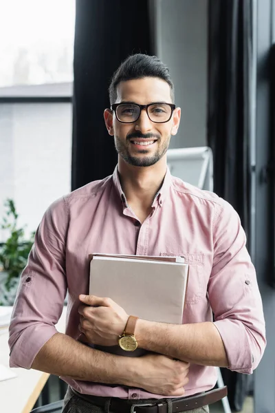 Feliz hombre de negocios árabe sosteniendo carpetas de papel en la oficina - foto de stock