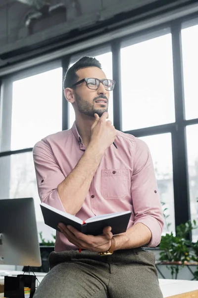 Pensive arabian businessman holding pen and notebook in office — Stock Photo