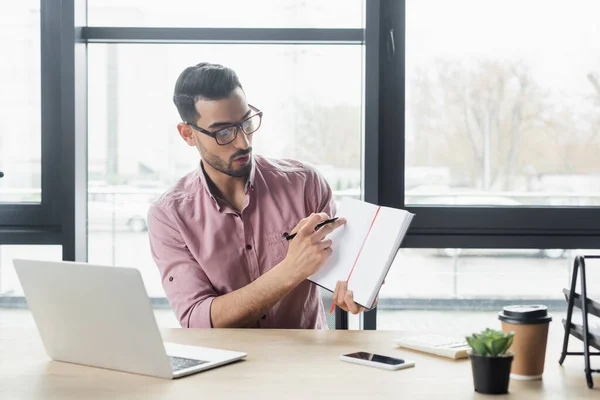 Arabe homme d'affaires pointant vers ordinateur portable pendant le chat vidéo sur ordinateur portable dans le bureau — Photo de stock