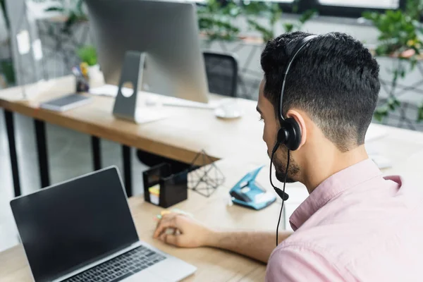 Hombre de negocios árabe con auriculares durante el chat de vídeo en el ordenador portátil en la oficina - foto de stock