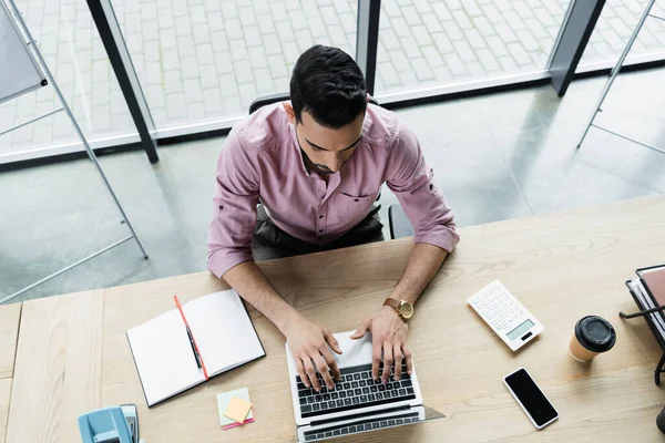 Overhead view of muslim businessman using laptop near calculator and notebook in office — Stock Photo