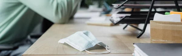 Vista recortada de la máscara médica en la mesa cerca de hombre de negocios borrosa en la oficina, pancarta - foto de stock