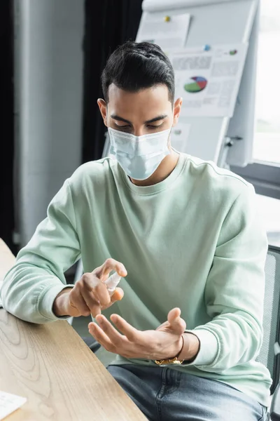 Muslim businessman in medical mask using hand sanitizer in office — Stock Photo