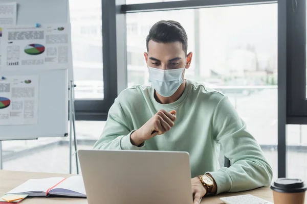 Homem de negócios árabe em máscara médica usando laptop perto notebook no escritório — Fotografia de Stock