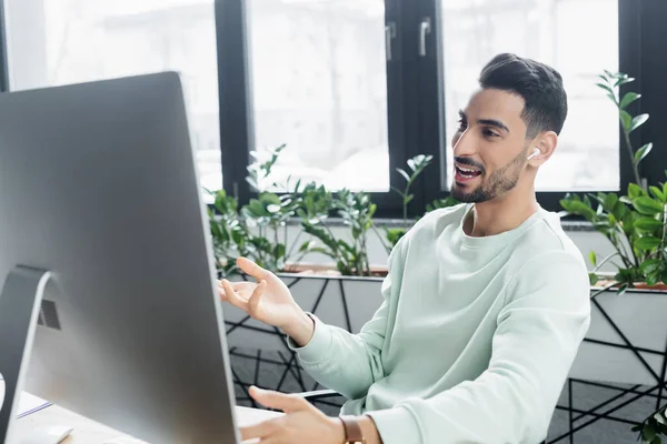 Positive muslim businessman in earphone having video call on computer in office — Stock Photo