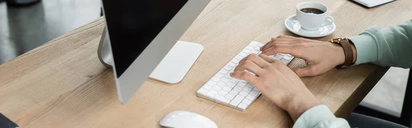 Vista ritagliata di uomo d'affari utilizzando la tastiera del computer vicino a tazza di caffè in ufficio, banner — Foto stock