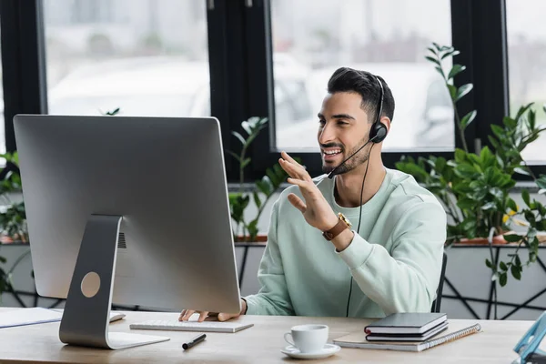 Uomo d'affari musulmano positivo in cuffia con video chat sul computer in ufficio — Foto stock