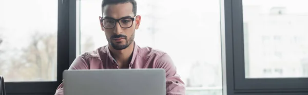 Arabischer Geschäftsmann mit Brille blickt auf Laptop im Büro, Banner — Stockfoto