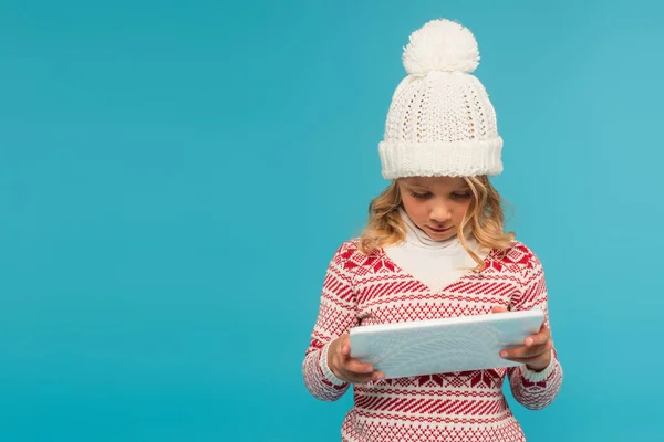 Enfant en chapeau chaud et pull avec ornement en utilisant une tablette numérique isolée sur bleu — Photo de stock