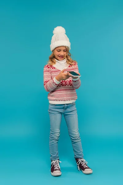 Piena lunghezza vista di ragazza positiva in maglione caldo invio messaggio vocale su blu — Foto stock