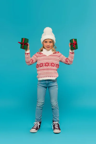 Full length view of kid in sweater and jeans showing green gift boxes on blue — Stock Photo
