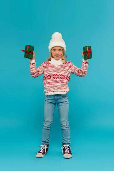 Full length view of kid in sweater and jeans showing green gift boxes on blue — Stock Photo