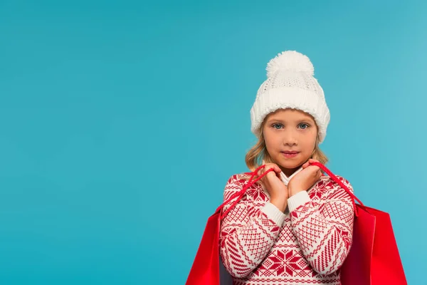 Mädchen in Strickmütze und Pullover mit Ornament hält Einkäufe isoliert auf blau — Stockfoto