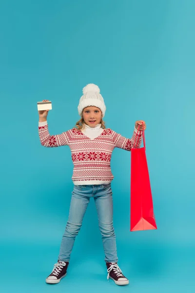 Vue pleine longueur de fille à la mode avec carte de crédit et sac à provisions sur bleu — Photo de stock