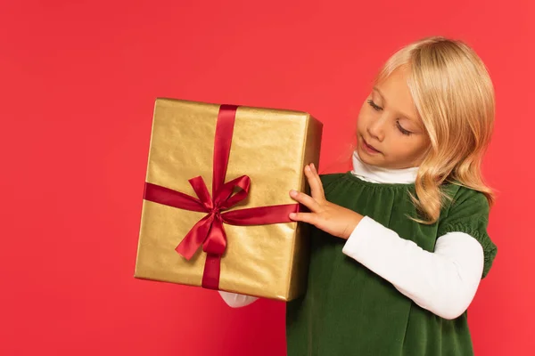 Girl in green dress looking at present in golden wrapping paper on red — Stock Photo