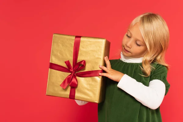 Ragazza in abito verde guardando presente in carta da imballaggio dorata su rosso — Foto stock