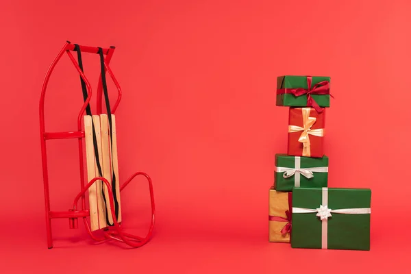 Stack of multicolored gift boxes near sled on red — Stock Photo